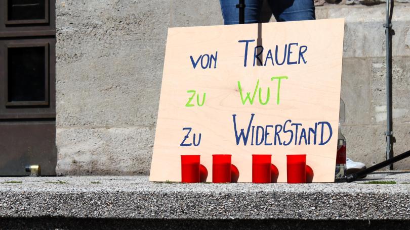 Von Trauer zu Wut zu Widerstand steht auf einem großen Schild, davor stehen vier rote Grabkerzen. Im Hintergrund ist das Mikrofon für die Redebeiträge erkennbar.